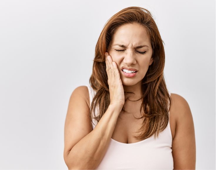 How a Bad Bite Can Lead to TMJ and Jaw Pain - navadiadentalclinic A woman with a pained expression holding her jaw, illustrating the facial pain and discomfort associated with TMJ/TMD, which is often a result of a bad bite (malocclusion).